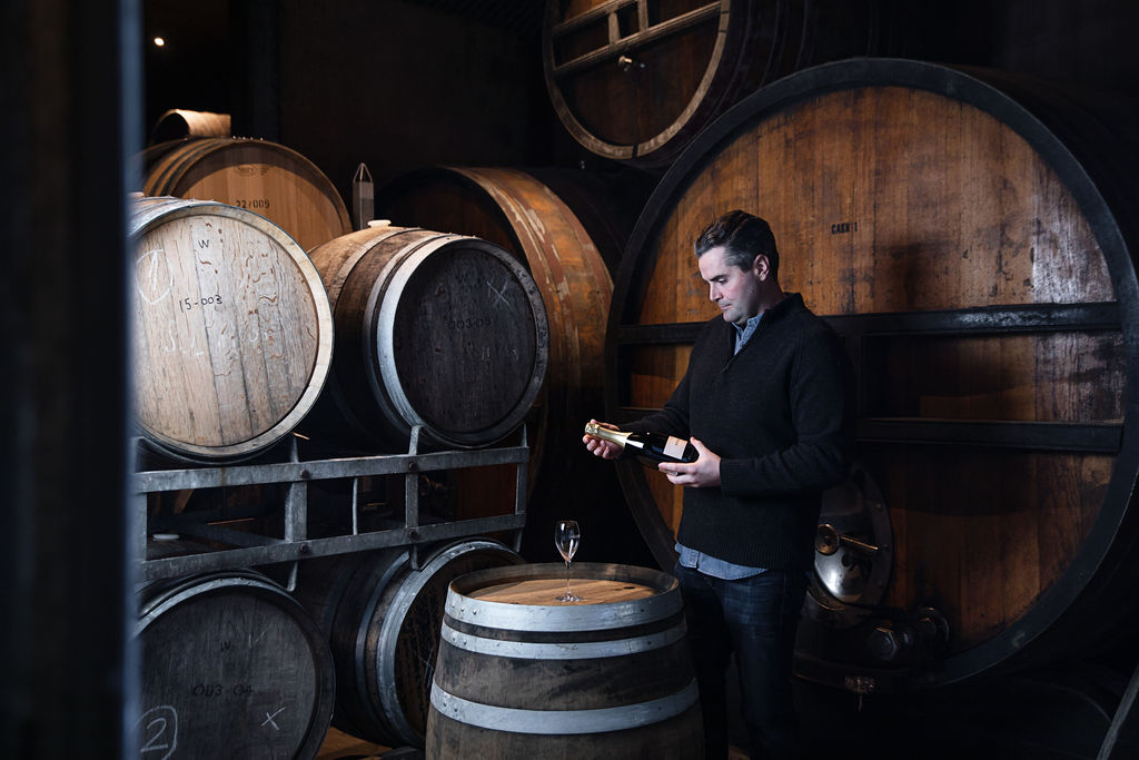 Winemaker inspecting a bottle of wine surrounded by barrels